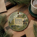A round ornament with a painting of a historical scene, featuring a soldier on horseback, a cannon, and a house, hangs on a wooden surface.
