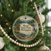 A round ornament hanging on a Christmas tree, featuring a scenic landscape with mountains, trees, and a lake.