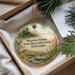 A decorative ornament with a scenic landscape of a lake, mountains, and a bird, hanging from a string.