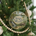 A round ornament hanging on a Christmas tree, featuring a scenic landscape with a waterfall and a cabin.
