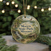 A round ornament with a scenic image of a waterfall and a cabin, surrounded by greenery, hangs in front of a blurred background with twinkling lights.