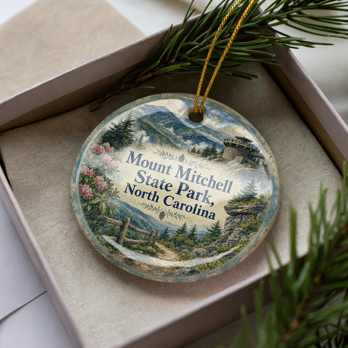 A decorative ornament featuring a scenic landscape of Mount Mitchell State Park in North Carolina, with a mountain, pine trees, and a path leading through the area.