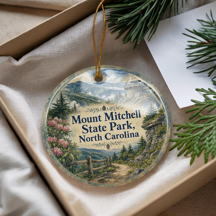 A decorative ornament with a scenic mountain landscape and pine trees, featuring the text "Mount Mitchell State Park, North Carolina" on it.