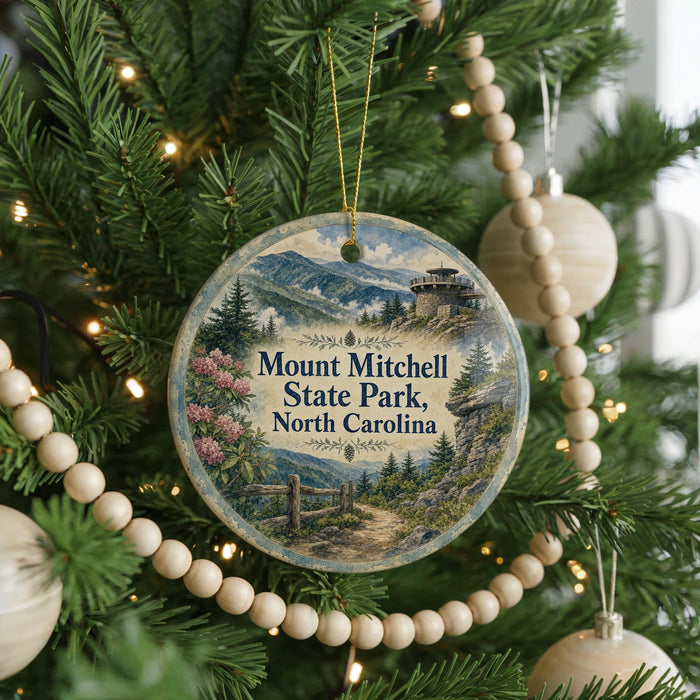 A round ornament hanging on a Christmas tree, featuring a scenic landscape with mountains and pine trees.