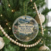 A round ornament hanging on a Christmas tree, featuring a scenic landscape with mountains and pine trees.