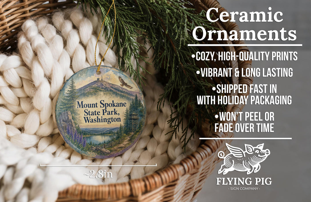 Ceramic ornaments, featuring a painting of Mount Spokane State Park in Washington, are displayed in a basket with pine branches.