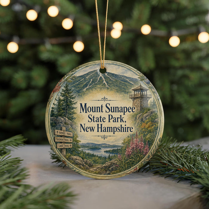 A decorative ornament featuring a scenic image of Mount Sunapee State Park in New Hampshire, with a lighthouse and mountains in the background.