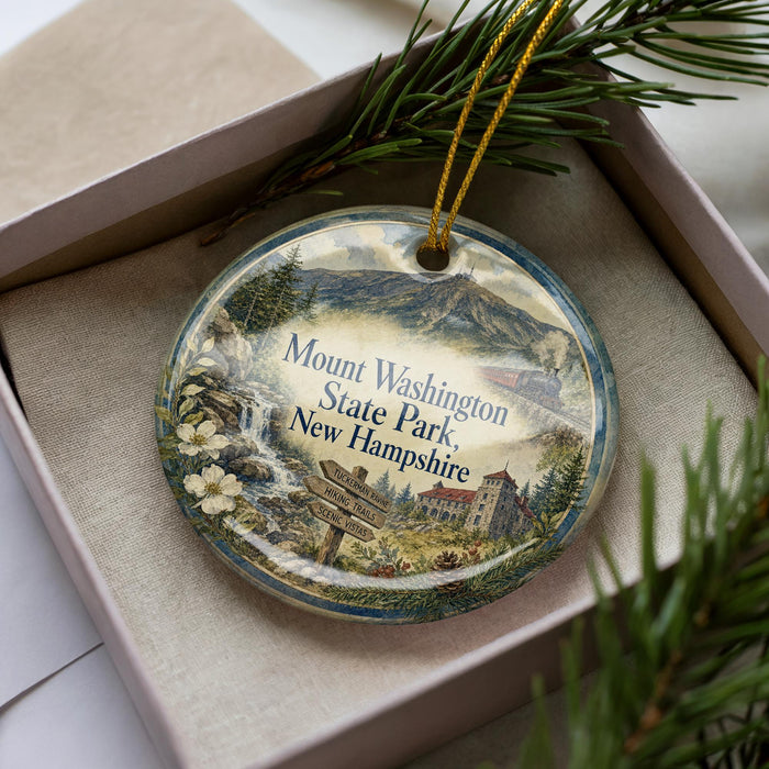 A decorative ornament featuring a scenic landscape of Mount Washington State Park, New Hampshire, with a mountain, pine trees, and a signpost.