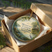 A round ornament in a wooden box, featuring a scenic landscape with a bird and trees, with the text "Mousetail Landing State Park, Tennessee" printed on it.