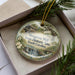 A decorative ornament in a box, featuring a scenic image of Musgrove Mill, South Carolina.