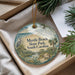 A decorative ornament with a beach scene and text, placed in a box with pine branches.
