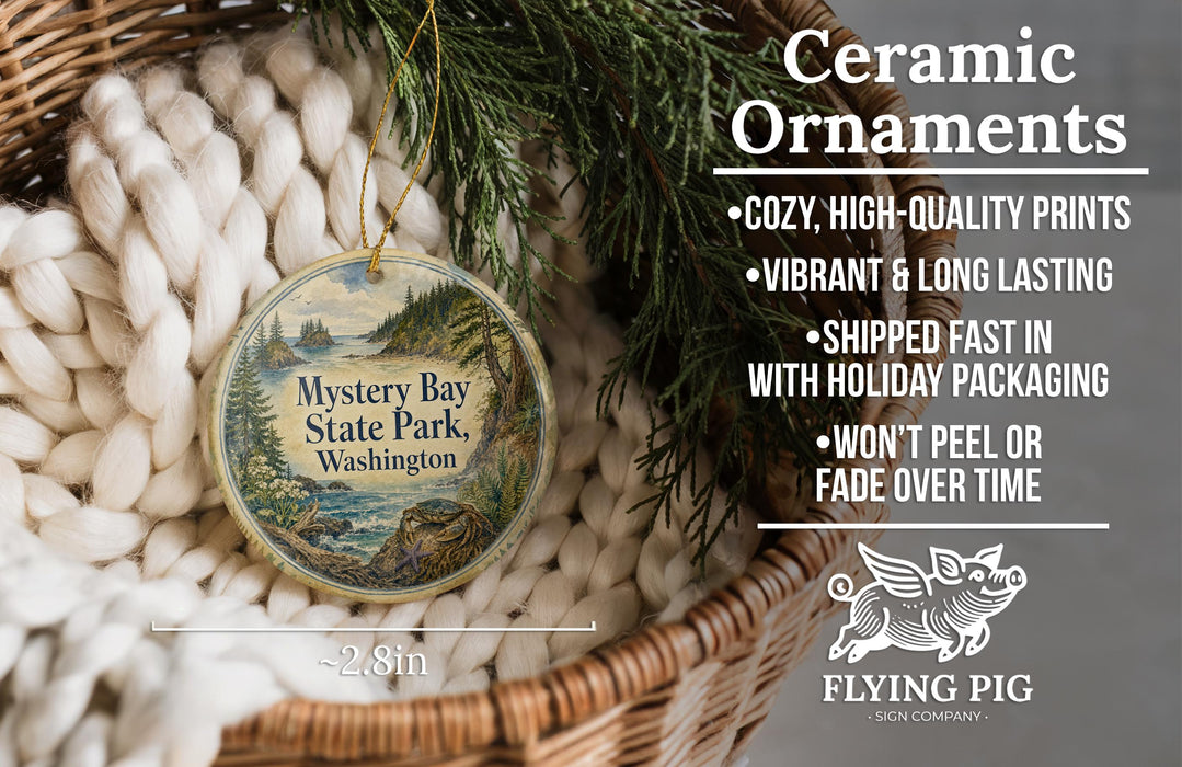 Ceramic ornaments, including a round ornament with a landscape scene, are displayed in a basket with a pine branch.