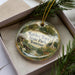 A decorative ornament in a box, featuring a scenic image of Natchez Trace State Park in Tennessee.