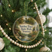 A round ornament hanging on a Christmas tree, featuring a scenic image of a park with a river and trees.