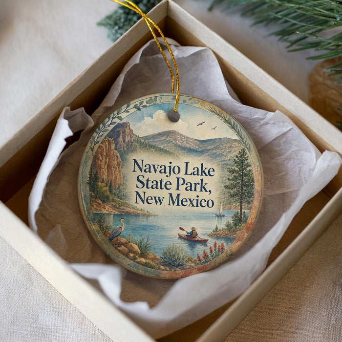 A decorative ornament in a box, featuring a scenic landscape with mountains, a lake, and a person kayaking.