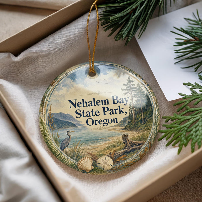 A decorative ornament with a scenic landscape of Nehalem Bay State Park, Oregon, featuring a bird, pine trees, and a body of water.