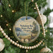 A round ornament hanging on a Christmas tree, featuring a scenic landscape with a lake, mountains, and a bird.