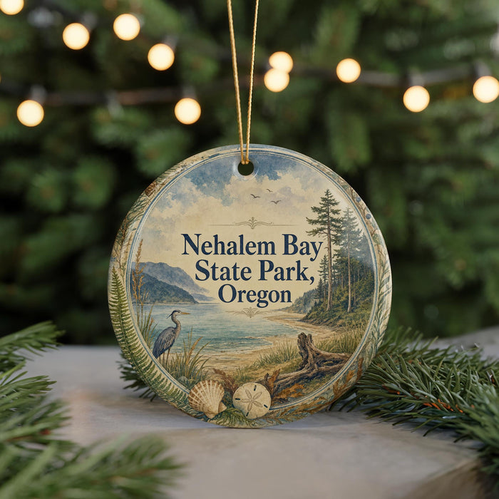 A round ornament with a scenic landscape of a lake, mountains, and trees, featuring a bird and a heron, is displayed on a table with a blurred background of a Christmas tree and lights.