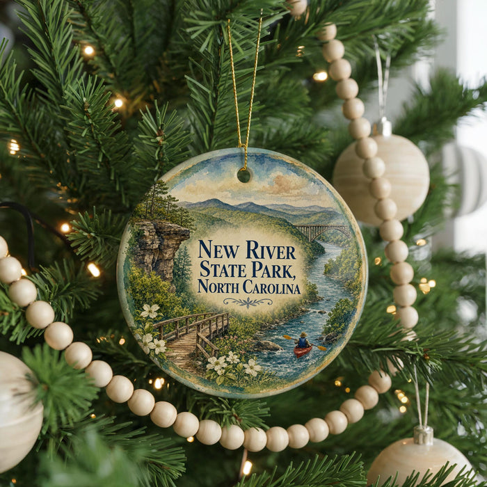 A Christmas tree ornament featuring a scenic image of the New River State Park in North Carolina, with a wooden bridge and a person in a red kayak.