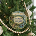 A Christmas tree ornament featuring a scenic image of the New River State Park in North Carolina, with a wooden bridge and a person in a red kayak.