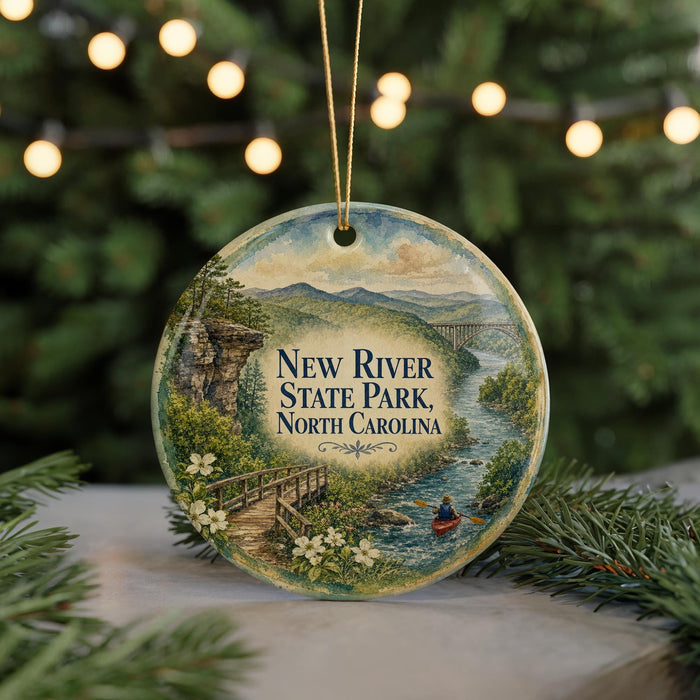 A decorative ornament featuring a scenic landscape with a river, bridge, and a person kayaking, hanging on a string.