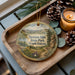 A wooden tray with a decorative ornament featuring a scenic landscape of Newton Hills State Park, South Dakota, and pine cones.