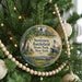 A round ornament hanging on a Christmas tree, featuring a scenic landscape with a monument and a cannon, surrounded by a beaded garland.