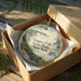 A decorative ornament in a box, featuring a scenic image of Niagara Falls, New York.
