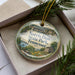 A decorative ornament with a scenic image of Norris Dam State Park, Tennessee, displayed in a box with pine branches.