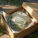A decorative ornament in a box, featuring a scenic image of a park with a river and buildings, with the text "NORRIS DAM STATE PARK TENNESSEE" printed on it.