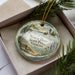 A decorative ornament in a box, featuring a scenic image of North Hero State Park in Vermont.