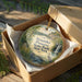 A decorative ornament in a wooden box, featuring a scenic landscape with a waterfall and greenery.
