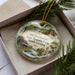 A decorative ornament with a scenic image of Old Dorchester State Historic Park, South Carolina, displayed in a box with pine branches.
