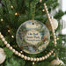 A round ornament hanging on a Christmas tree, featuring a scenic landscape with a river, mountains, and pine trees.