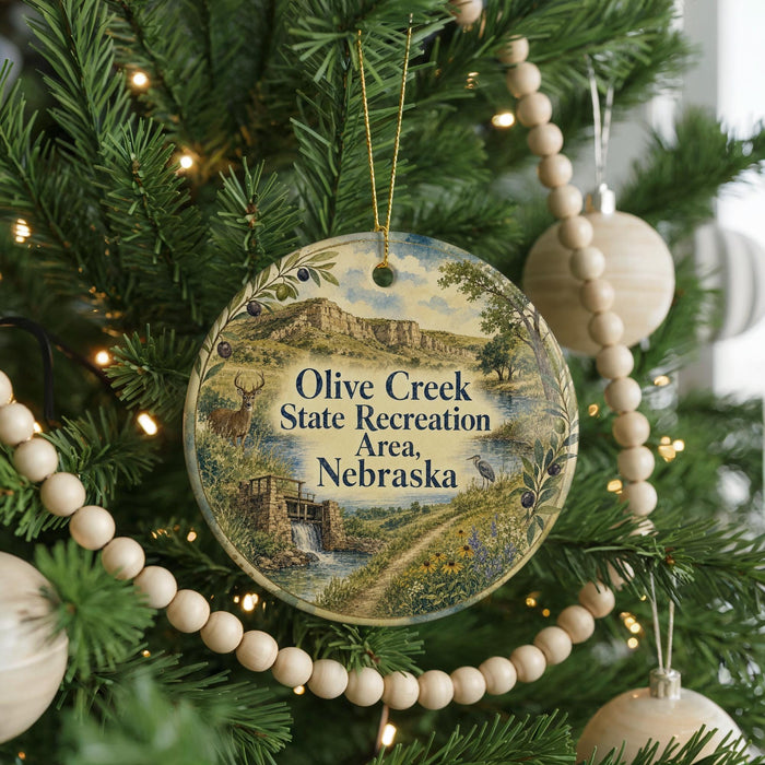 A round ornament hanging on a Christmas tree, featuring a scenic landscape with a river and mountains.