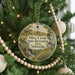 A round ornament hanging on a Christmas tree, featuring a scenic landscape with a river and mountains.