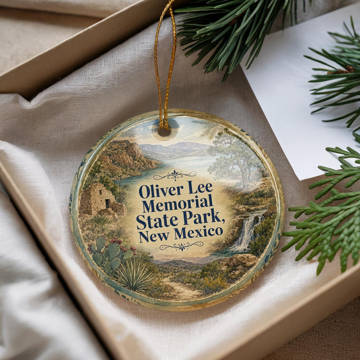 A decorative ornament with a landscape scene, featuring a river, mountains, and trees, is displayed in a box with pine branches.