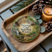 A decorative ornament featuring a scenic image of Onondaga Cave State Park, Missouri, with pine cones and a lit candle on a wooden tray.