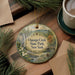 A decorative ornament with a scenic image of Oquaga Creek State Park in New York, featuring a waterfall and pine trees, is displayed on a wooden surface alongside a cup of coffee and some papers.
