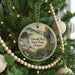 A round ornament hanging on a Christmas tree, featuring a scenic landscape with mountains, a river, and a bridge.