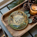 A wooden tray with a decorative ornament featuring a scenic image of Ozark Caves at Lake of the Ozarks, Missouri, and pine cones.