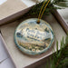 A decorative ornament in a box, featuring a scenic image of Pacific Beach State Park in Washington.