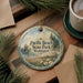 A decorative ornament with the text "Pacific Beach State Park, Washington" on it, surrounded by pine branches and a cup of coffee on a wooden surface.