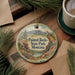 A decorative ornament featuring a scenic landscape of Painted Rocks State Park, Montana, with a bird perched on a rock. The ornament is placed on a wooden surface, surrounded by pine branches and a cup of coffee.