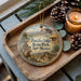 A decorative ornament featuring a cowboy on horseback, with the text "Pancho Villa State Park, New Mexico" displayed prominently. The ornament is placed on a wooden tray, surrounded by pine cones and a lit candle, creating a rustic and western-themed setting.