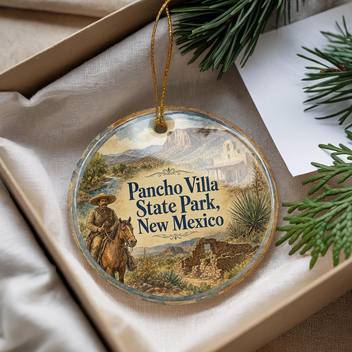 A decorative ornament with a cowboy on horseback and the text "Pancho Villa State Park, New Mexico" on it, placed in a box with pine branches.