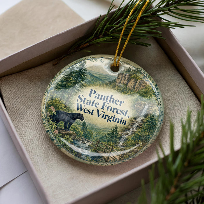 A decorative ornament in a box, featuring a scenic landscape with a black bear and a waterfall.