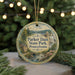 A round ornament with a scenic image of the park, featuring a waterfall and a house, is displayed on a table with pine branches in the background.