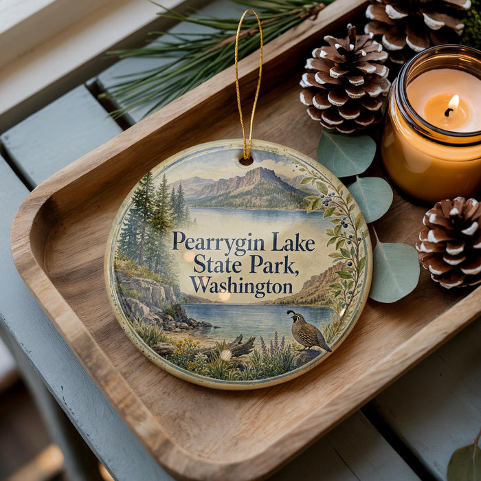 A decorative ornament with a scenic image of Pearyrgin Lake State Park, Washington, featuring a bird, pine cones, and a candle on a wooden tray.