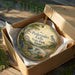 A decorative ornament in a wooden box, featuring a scenic landscape with a waterfall and flowers, with the text "Pedernales Falls State Park, Texas" printed on it.